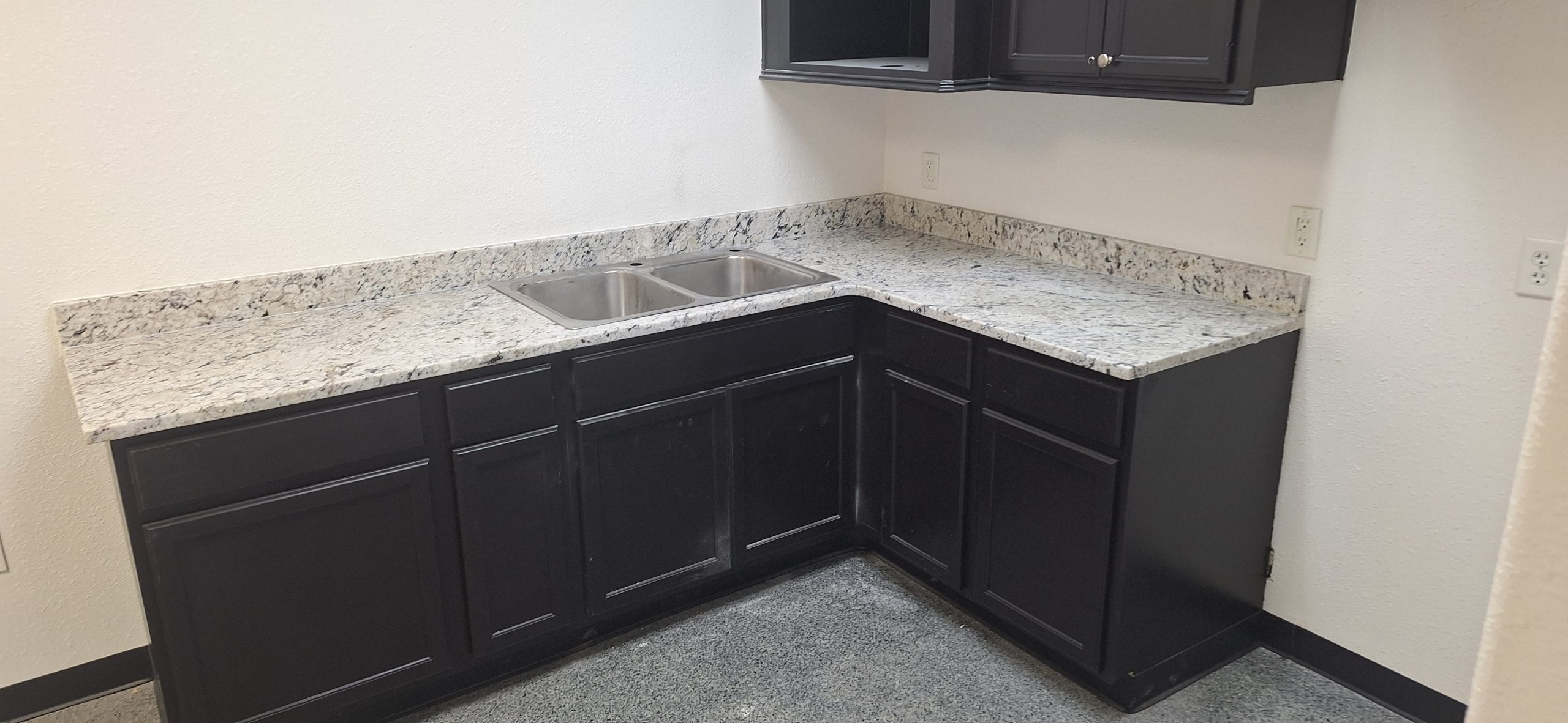 an l-shaped corner kitchen with dark cabinets and stone countertops