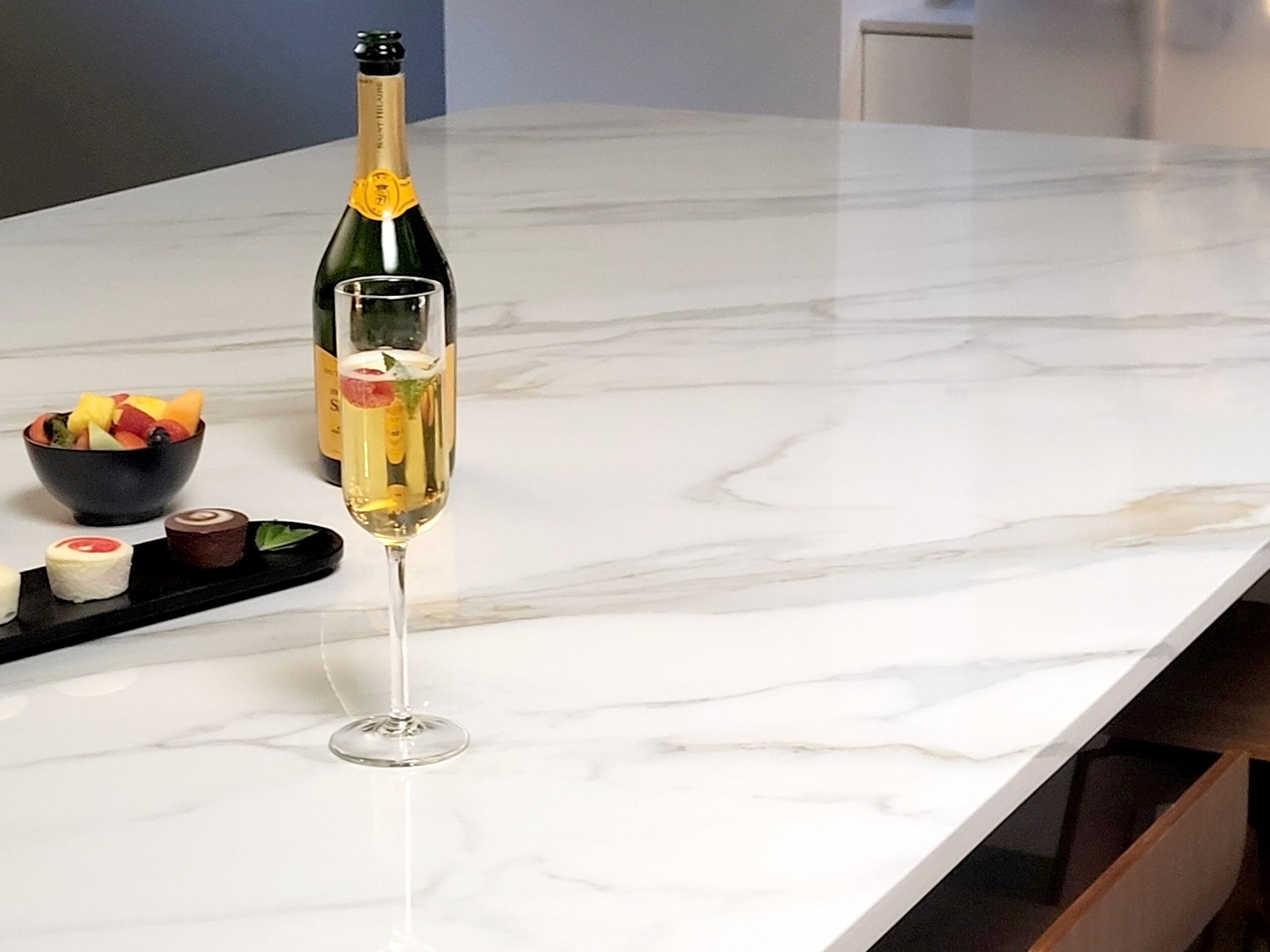 Close up of champagne glass and bottle on kitchen counter made with TERACANTO porcelain in the shade Calacatta.