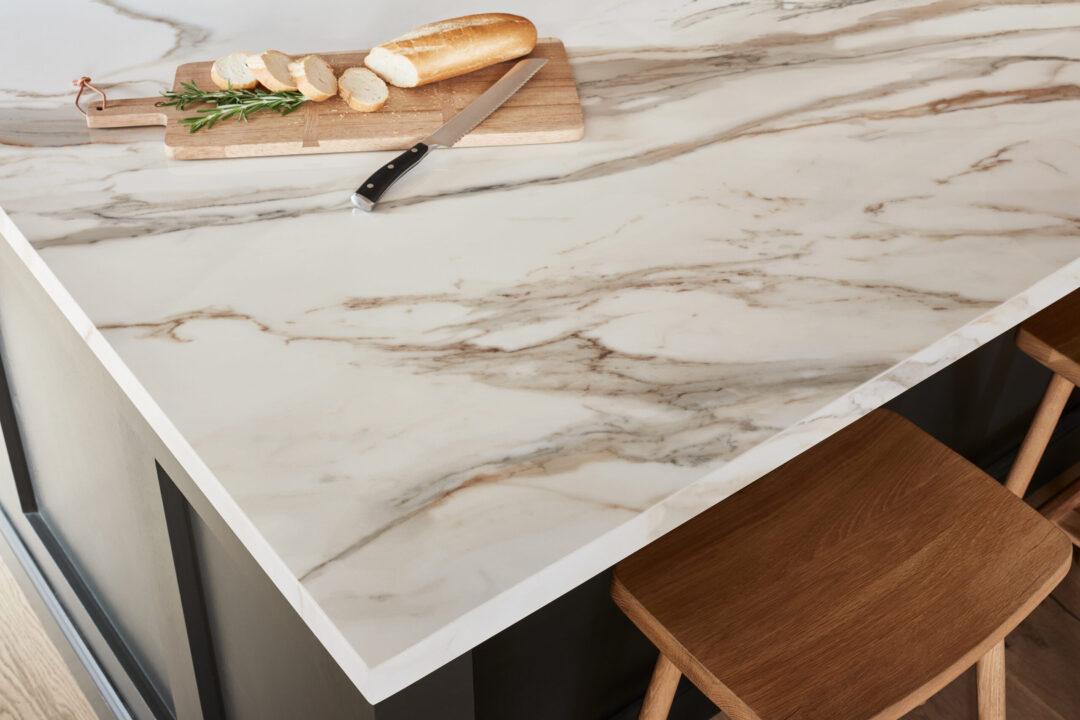 Closeup of the corner of a white and gold porcelain countertop edge with a plate of bread and knife on it.