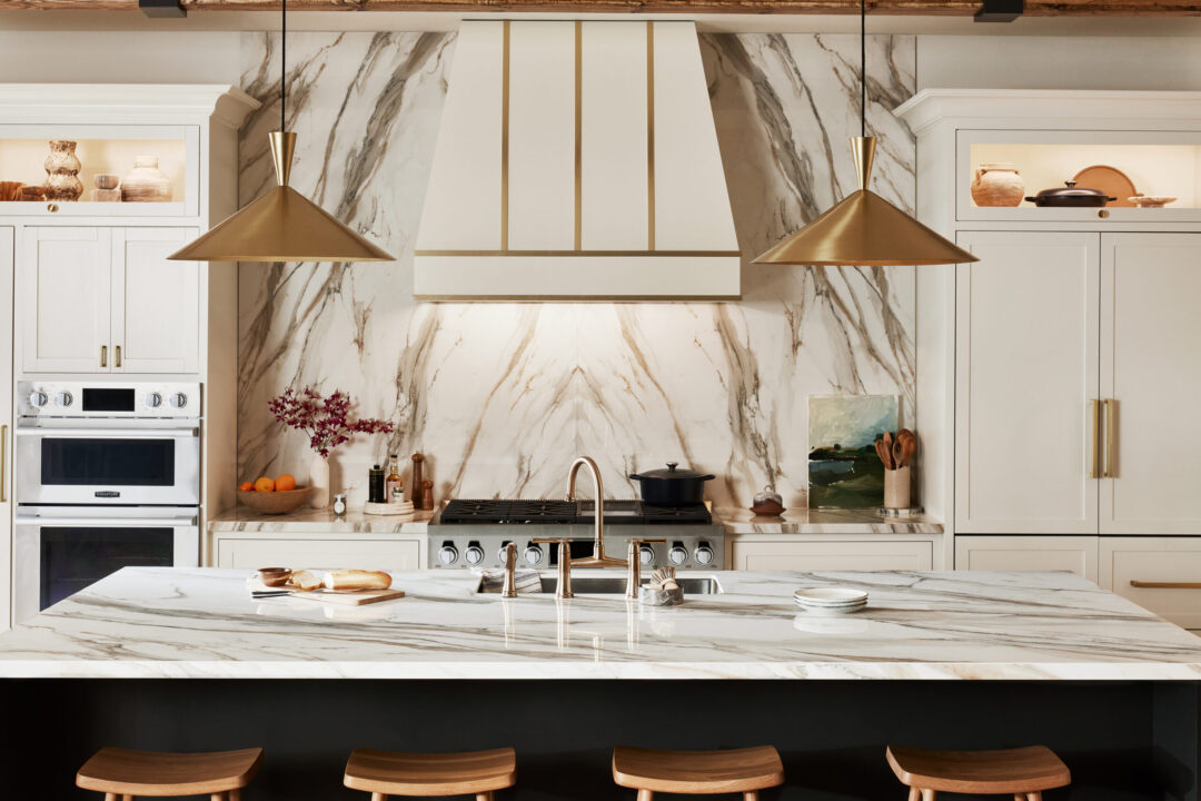 A luxurious white and gold kitchen with porcelain countertops, island, and backsplash.