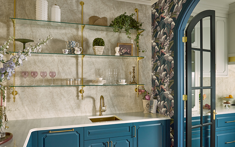A modern kitchen with a porcelain backsplash that covers the wall with floating shelves of decor and glassware. 