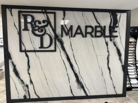 A commercial office porcelain slab wall with the R&D Marble logo on it.