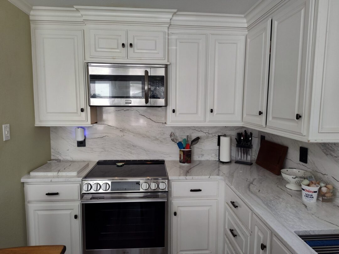 A newly renovated kitchen with white cabinetry and custom stone countertops and matching backsplash installed.