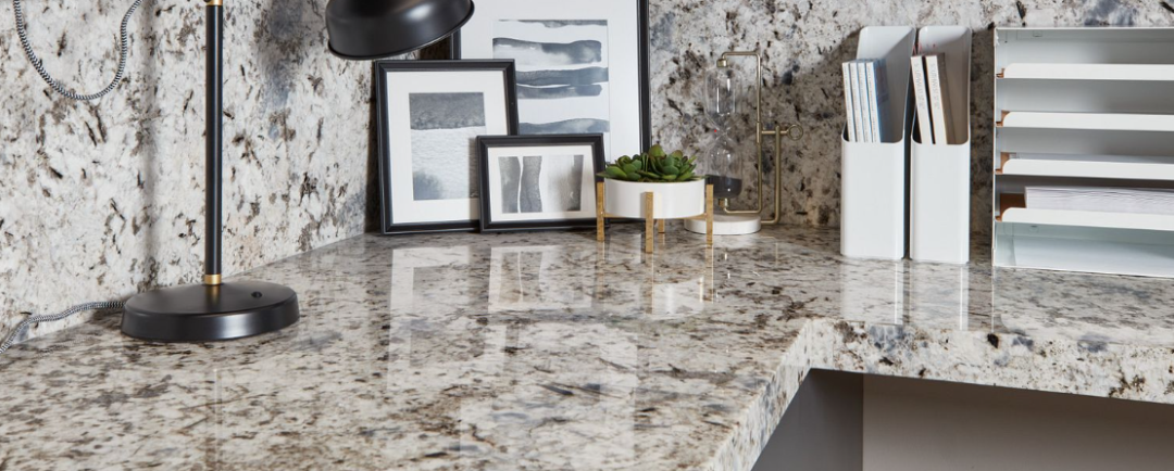 Close up of a kitchen corner granite countertop with backsplash and lamp, books, photo frames and other decor.