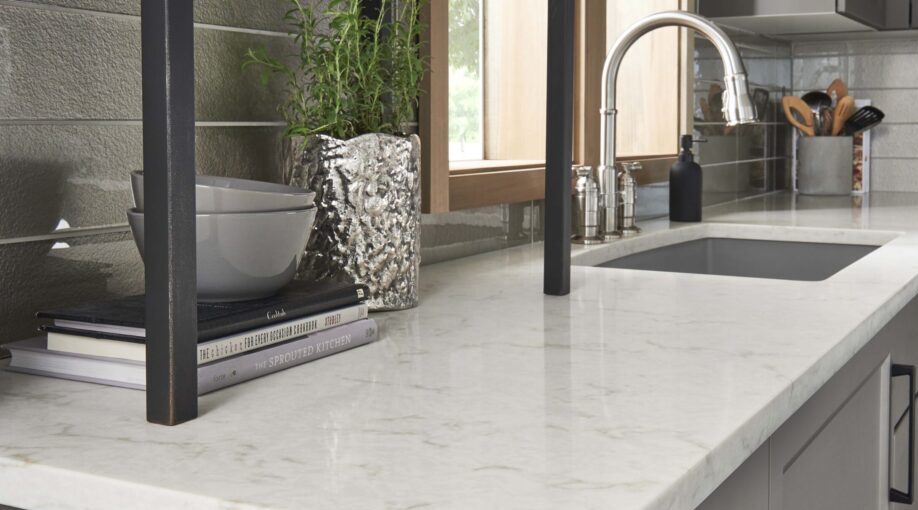 Close up of the corner of a beautiful white quartz kitchen countertop with a sink in the background and modern decor on the counter.